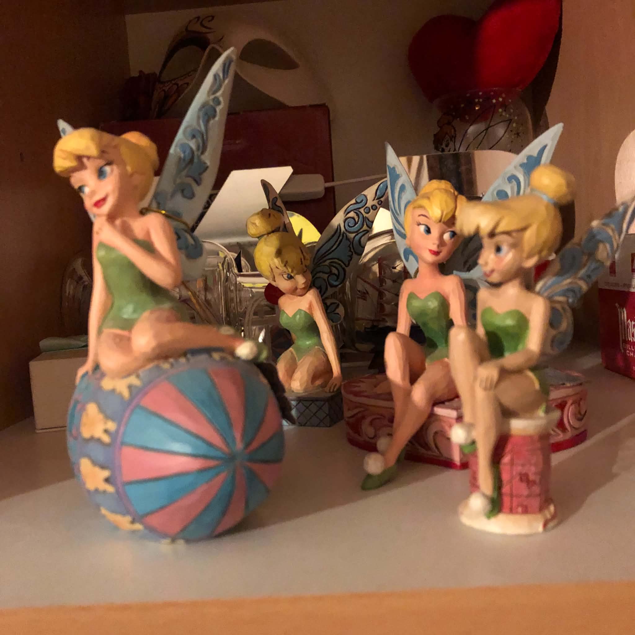 Four Tinkerbell statuettes on a display shelf.