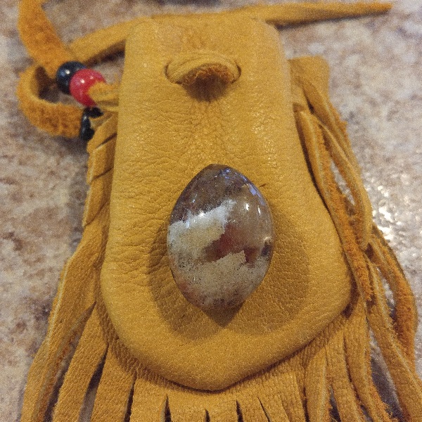 A brown leather medicine bag with leathert fringes hanging from it, and a clearish stone sitting on top.