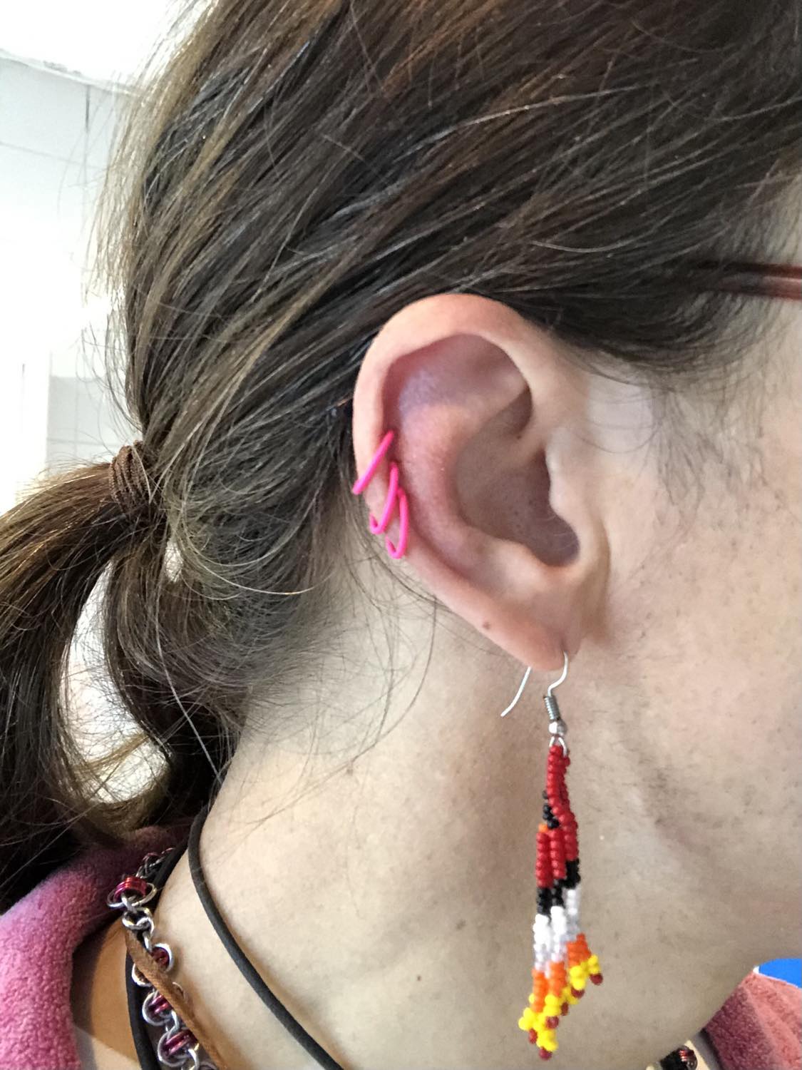 Kabutroid wearing three pink hoops in her helix piercings, and red indigenous beaded earrings in her initial lobe piercings.