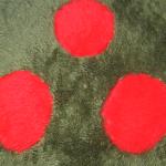 A green Metroid pillow, made out of green furry fabric with red orbs and white teeth.