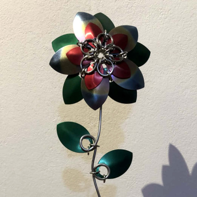 A five petal flower made from large and small scales, with green scales behind and as leaves down the steel wire stem.