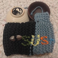 A knitted cupholder, with the cups removed and behind it, and the name Sushi partially visble on the front