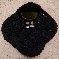 A large square of black fabric, made up of four compartments, with the upper one being partially opened to reveal a cup, with a brown rim and a green interior. It's on a white rug.