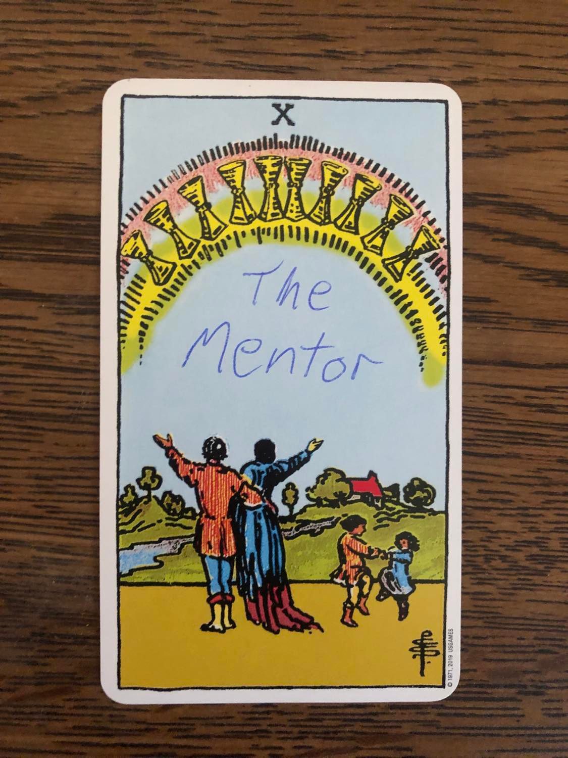 The ten of cups card with the mentor written on it, laying on a wooden desk.