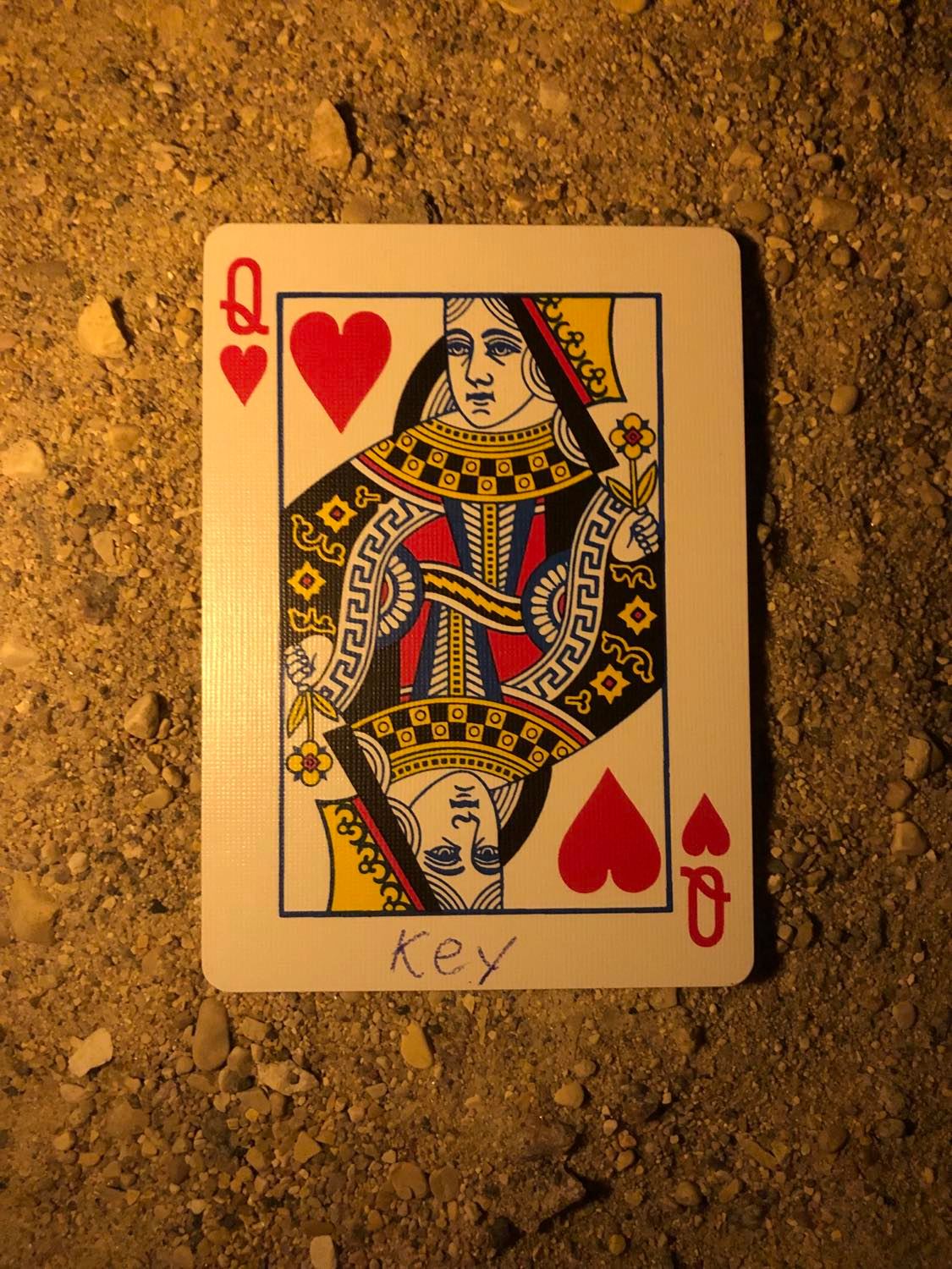 The queen of hearts with Key written on it, laying on the darkened soil.