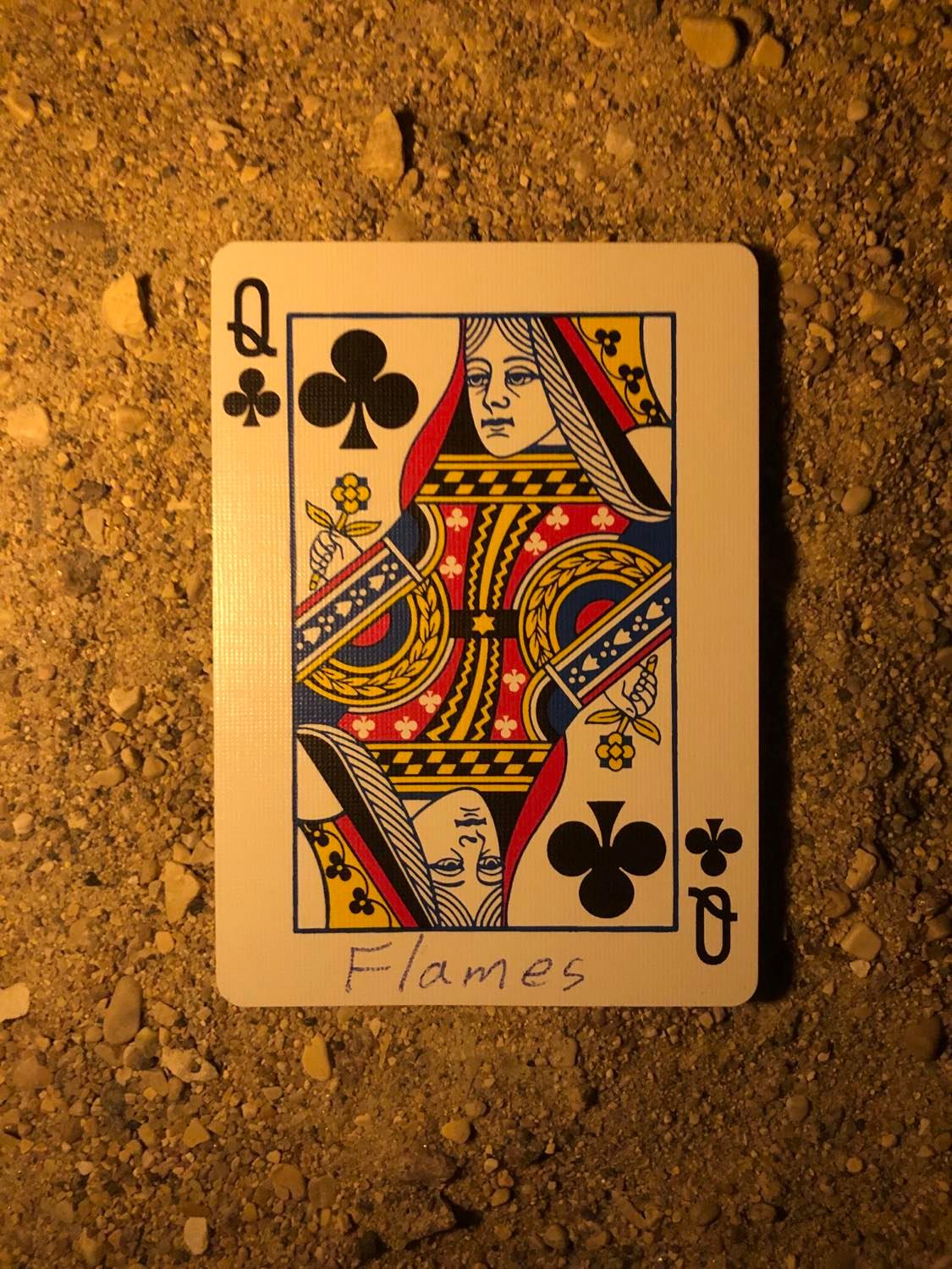 The queen of clubs with Flames written on it, laying on the darkened soil.