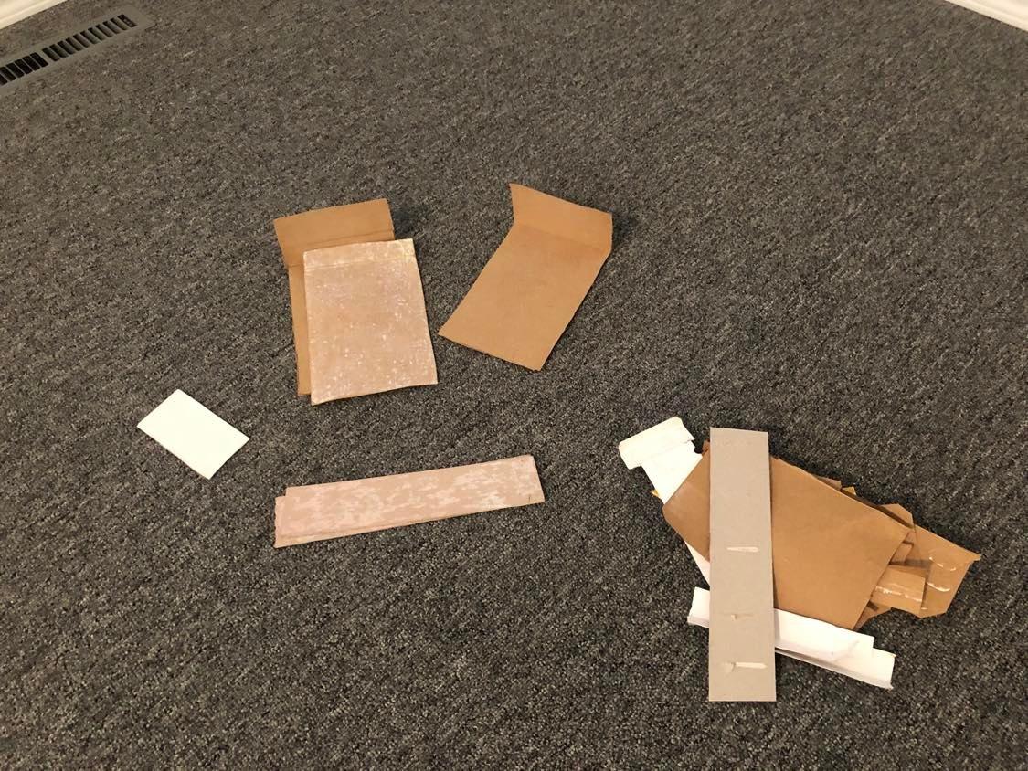 A scattering of cardboard, arranged to look somewhat like a face holding a smaller pile of scrap cardboard