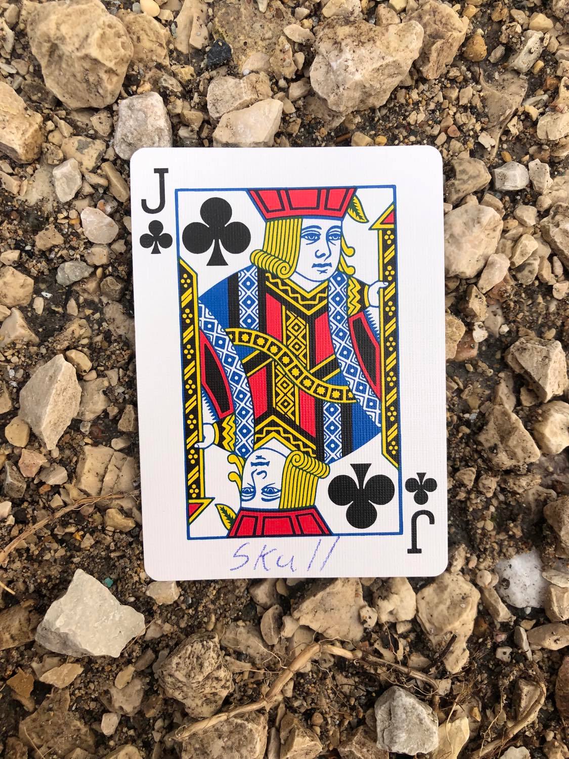 The jack of clubs with Skull written on it, laying on the gravel path.