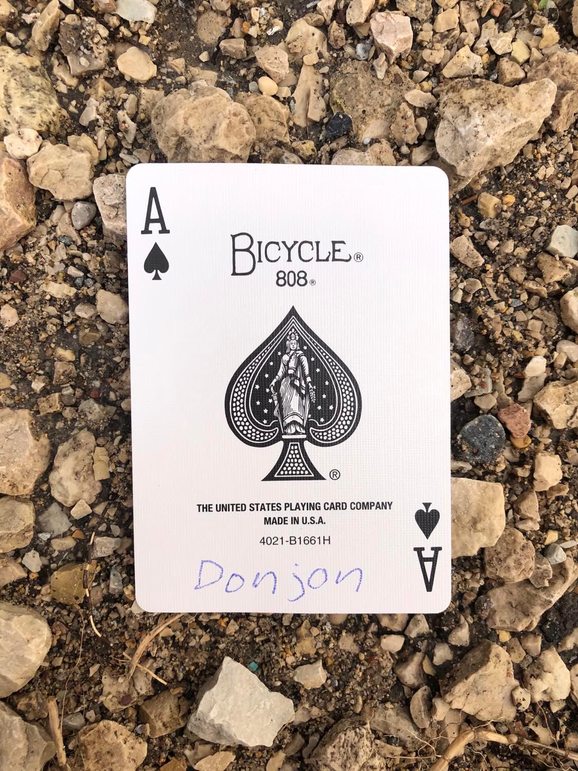 The ace of spades with Donjon written on it, laying on the gravel path.
