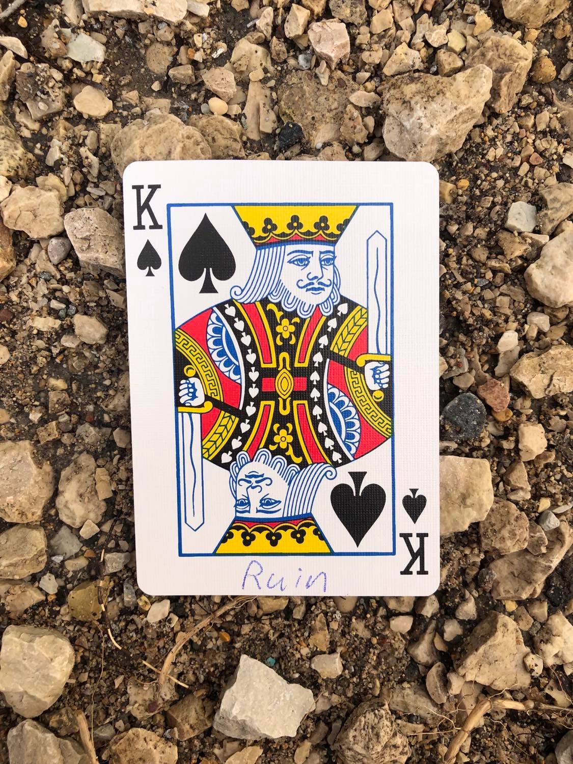 The king of spades with Ruin written on it, laying on the gravel path.
