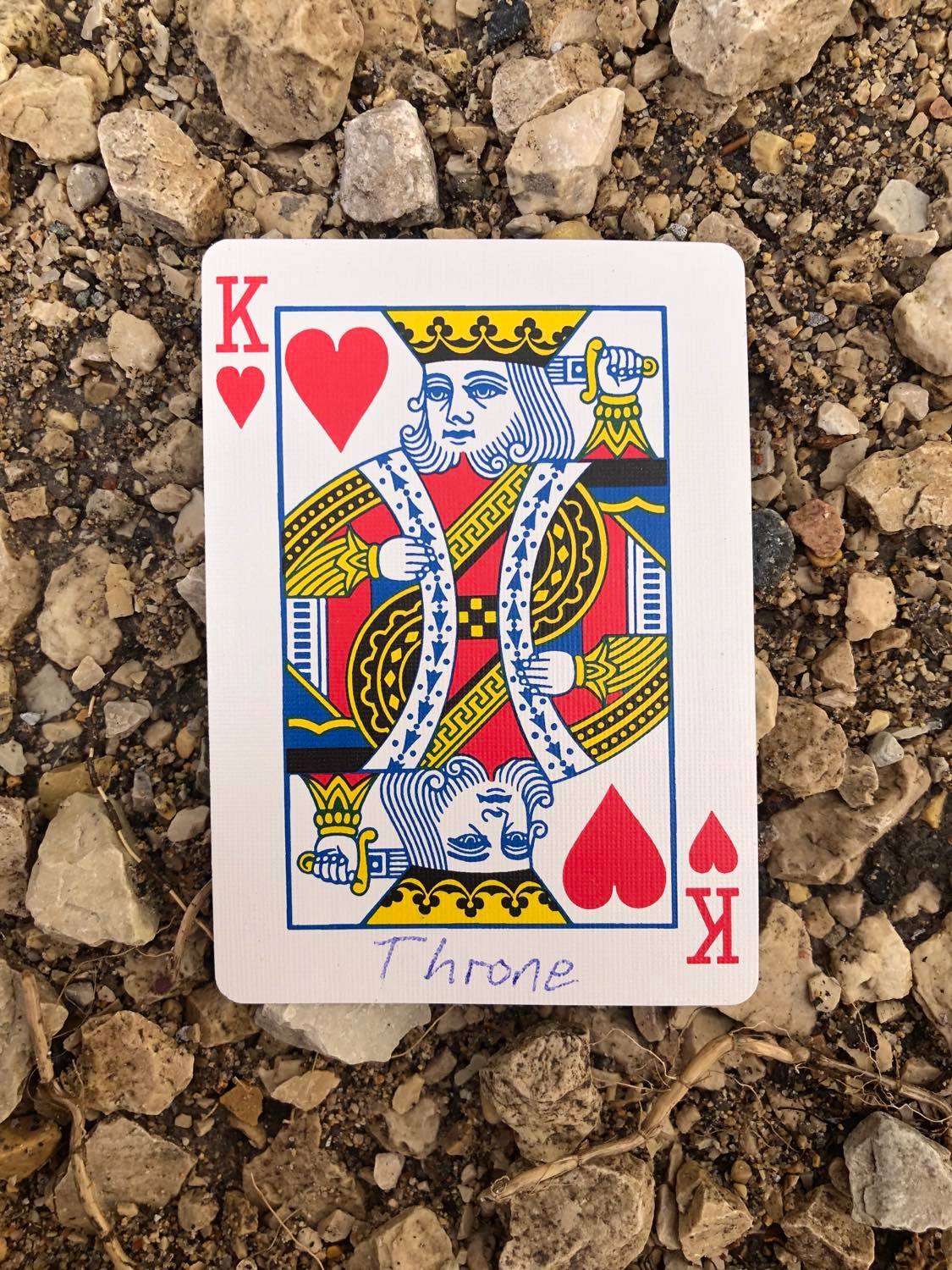 The king of hearts with Throne written on it, laying on the gravel path.