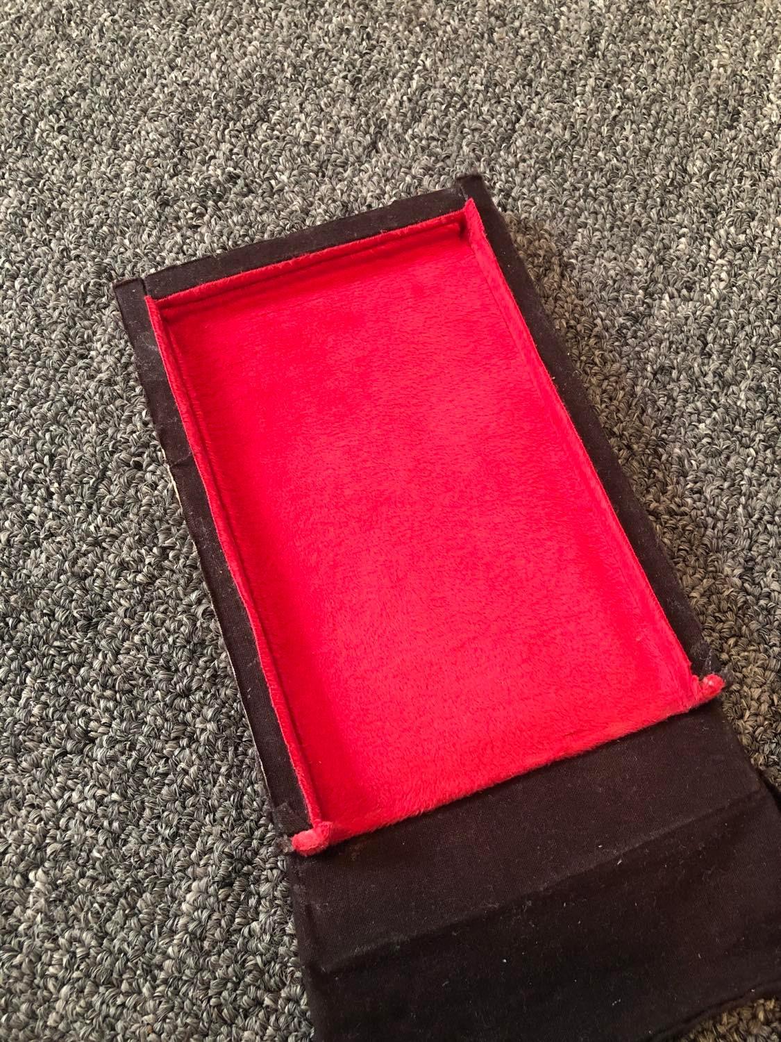 The red velvet lining of the box, appearing clean and flat. Think of it like, the box has had the top face of it removed, so basically an open box, except one side is a door. And the bottom face is hiding the cards