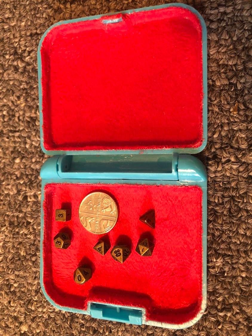 The sewing kit, emptied out and the inside lined with red fabric. The plastic exterior is light blue for now. Inside are the seven tiny metal dice, and a five pence piece to show size.