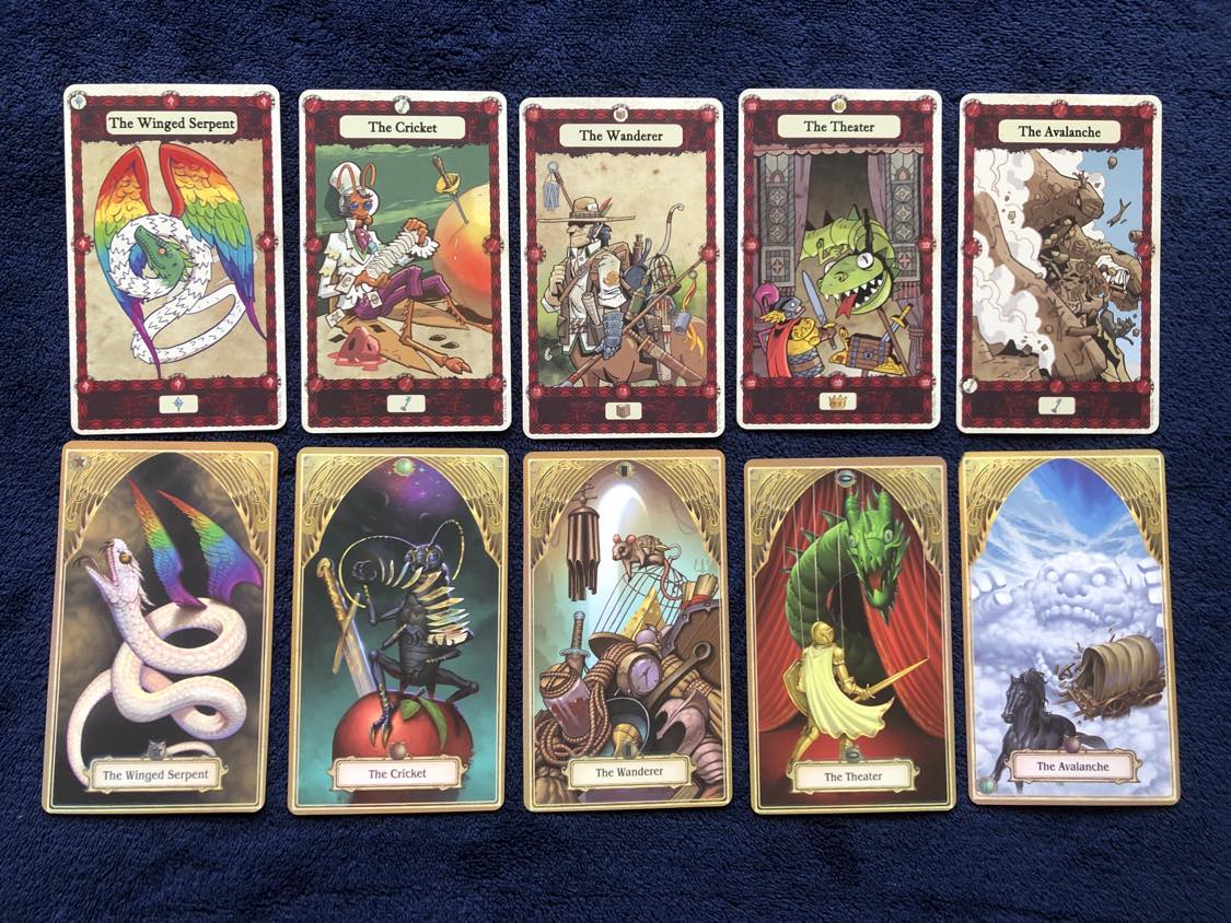 This picture shows comparisons between the 1e and 2e decks. The first shown is The Winged Serpent, the original, and all originals, being a more comic-style drawn white snake with a green head, with larger rainbow wings, still facing towards the top left. The newer version shows a much more elaborate fully white snake, with smaller rainbow wings. Second is The Cricket, which in the original shows a cricket with a white top hat and suit, playing with a deck of cards, sitting beside a large apple with a sword in it, and the newer version is a much more realistic looking cricket, without any suit, still playing with cards, sitting atop the apple with a much larger sword in it. The third is The Wanderer, which in 1e shows a travelling centaur carrying many items on their back, with just a plain slightly textured brown background, while the newer just shows a heaping pile of miscellaneous goods, rope, a clock, cheese in a bird cage, with a mouse on top, a shield, a helmet, chimes, and other items. The next card is The Theater, which shows a very comical, almost paper-cutout rendition of a fighter defending against a dragon emerging from behind curtains. No puppet strings are shown in the original. In 2e, it's a much more realistic fighter in golden armour, possibly the same as from The Paladin card, defending against a much more detailed green dragon emerging from behind curtains, but puppet strings are shown connected to both. In the last card shown, The Avalanche, the 1e version shows a rocky cliffside becoming a large golem, throwing a horse and cart from the path off a cliff, while the 2e version shows a black horse and cart being attacked and broken by a cloud giant behind them, atop a cloudy ground, much different from the original.