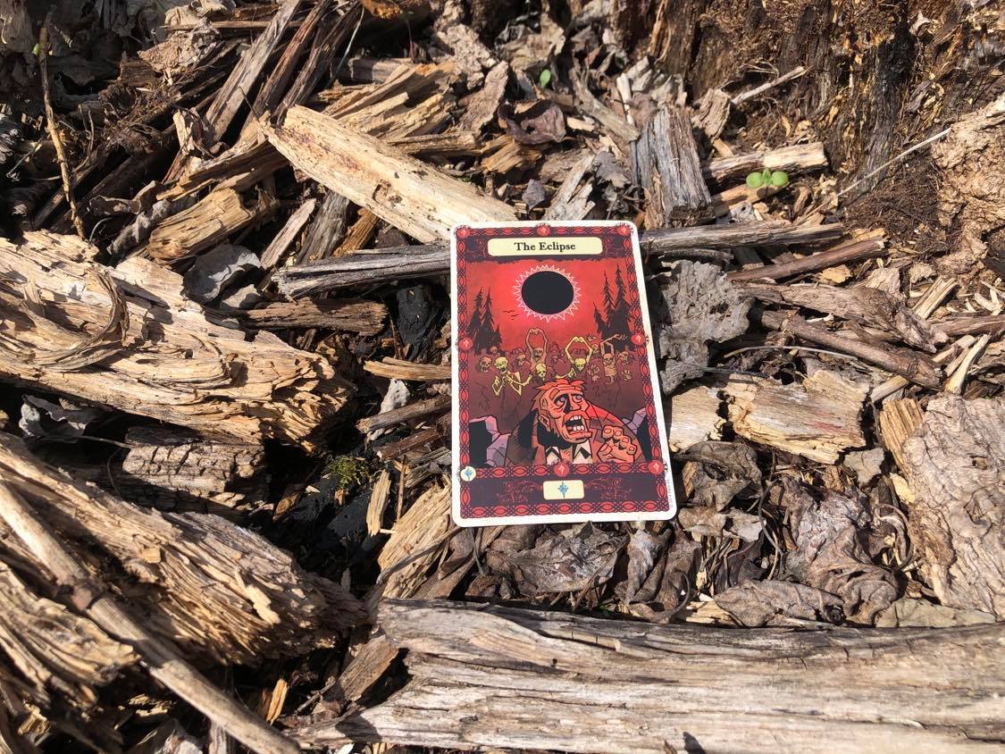 A man blinded by an eclipse, the card laying on the forest debris.