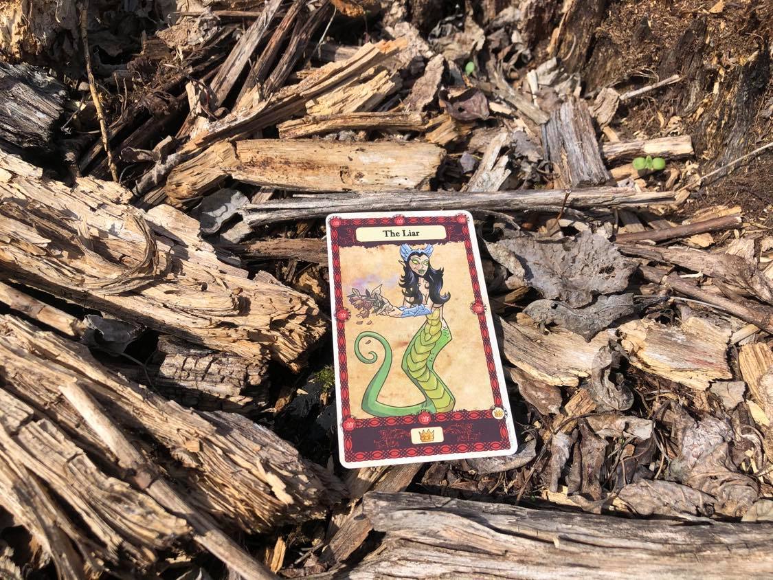A naga holding a decayed bouquet of flowers, the card laying on the forest debris.