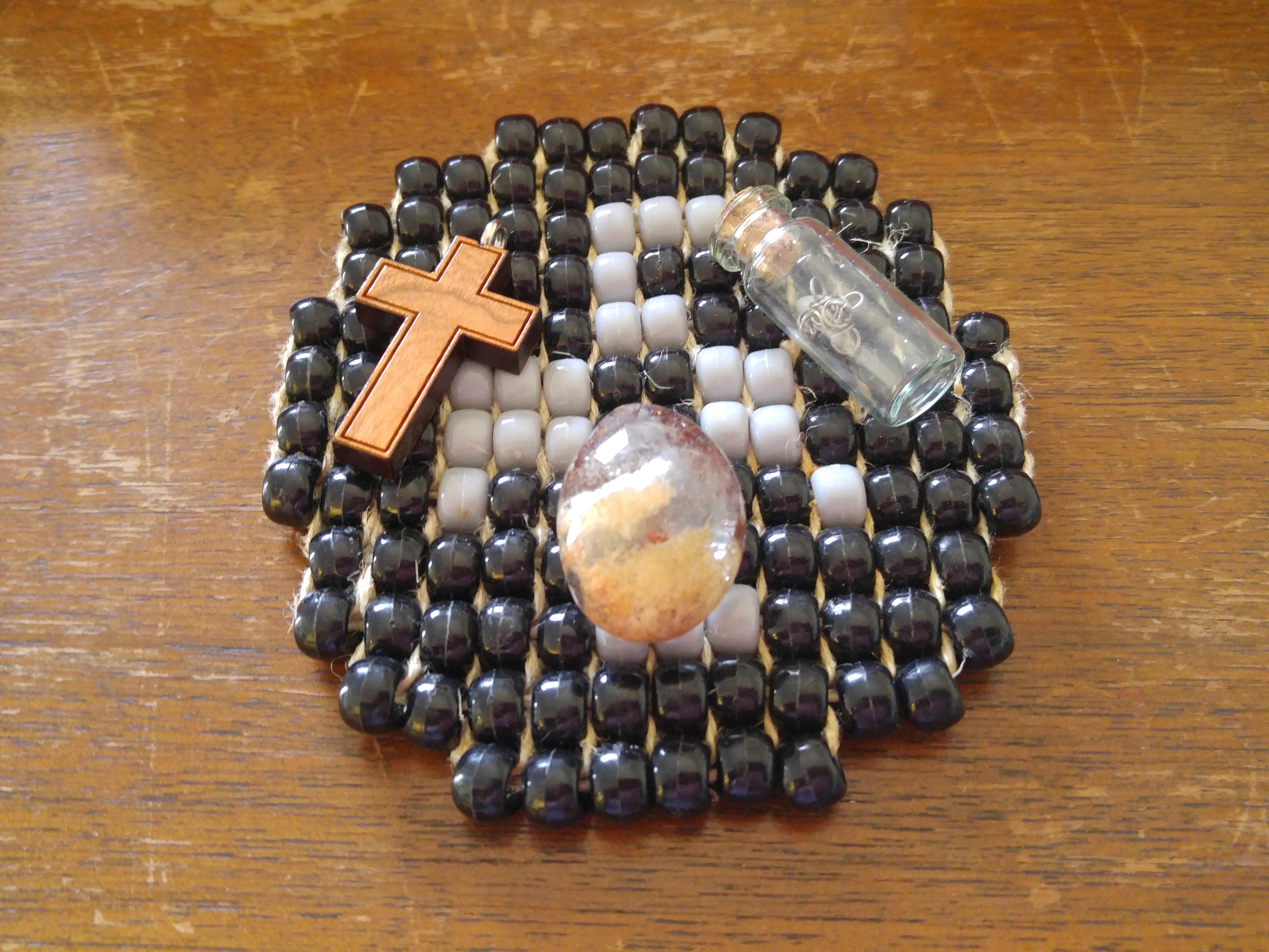 The cross, rock, and glass bottle sitting on top of a beaded coaster.