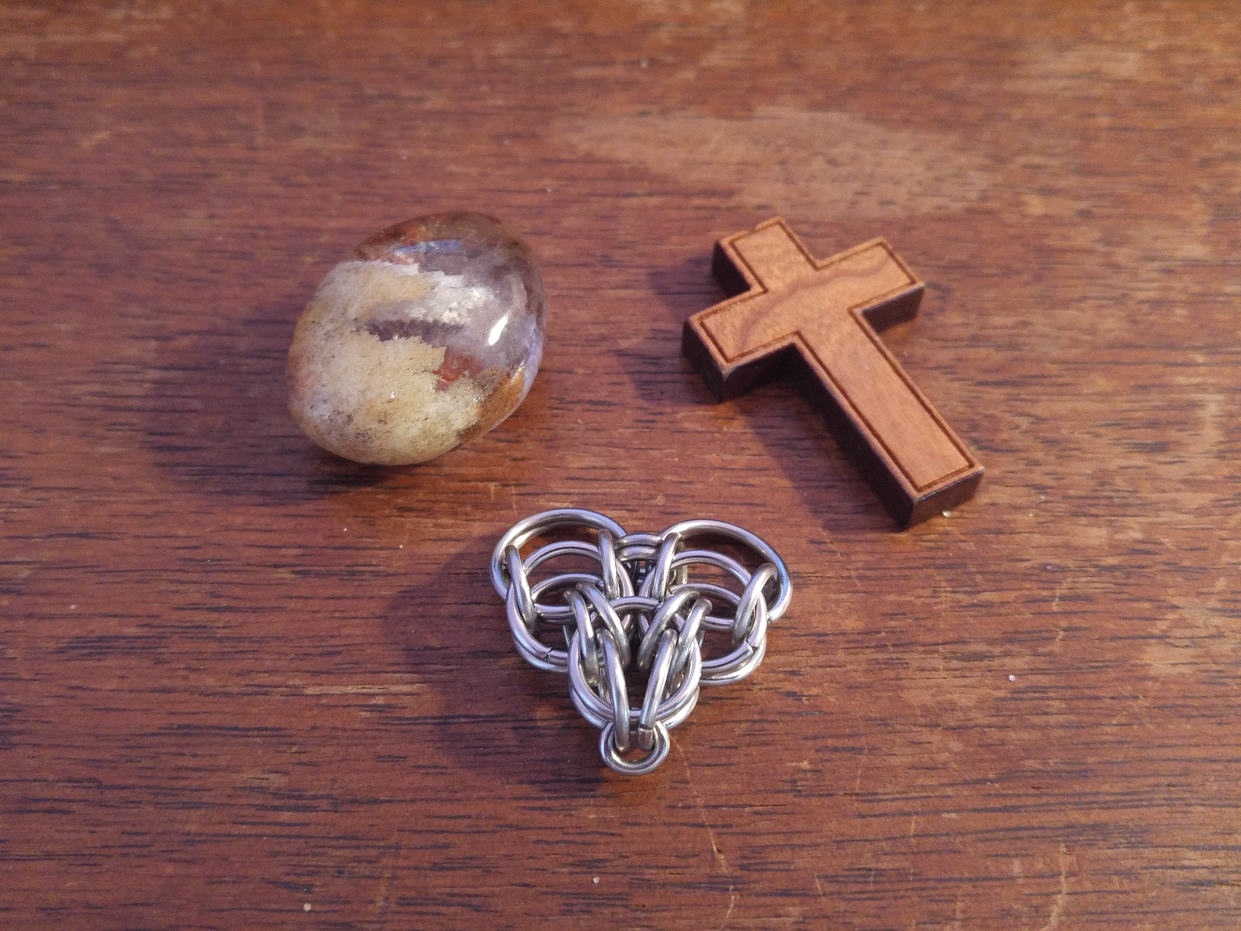 The rock, sitting beside a chainmaille heart, and the cross on a wooden desk.