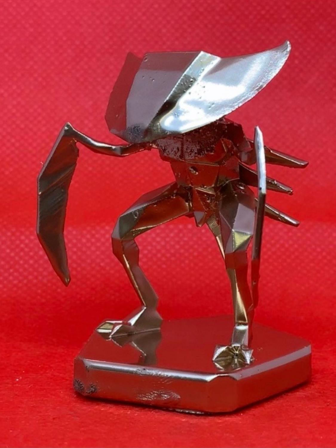 A shiny golden Kabutops figurine on a base, with a red backdrop.