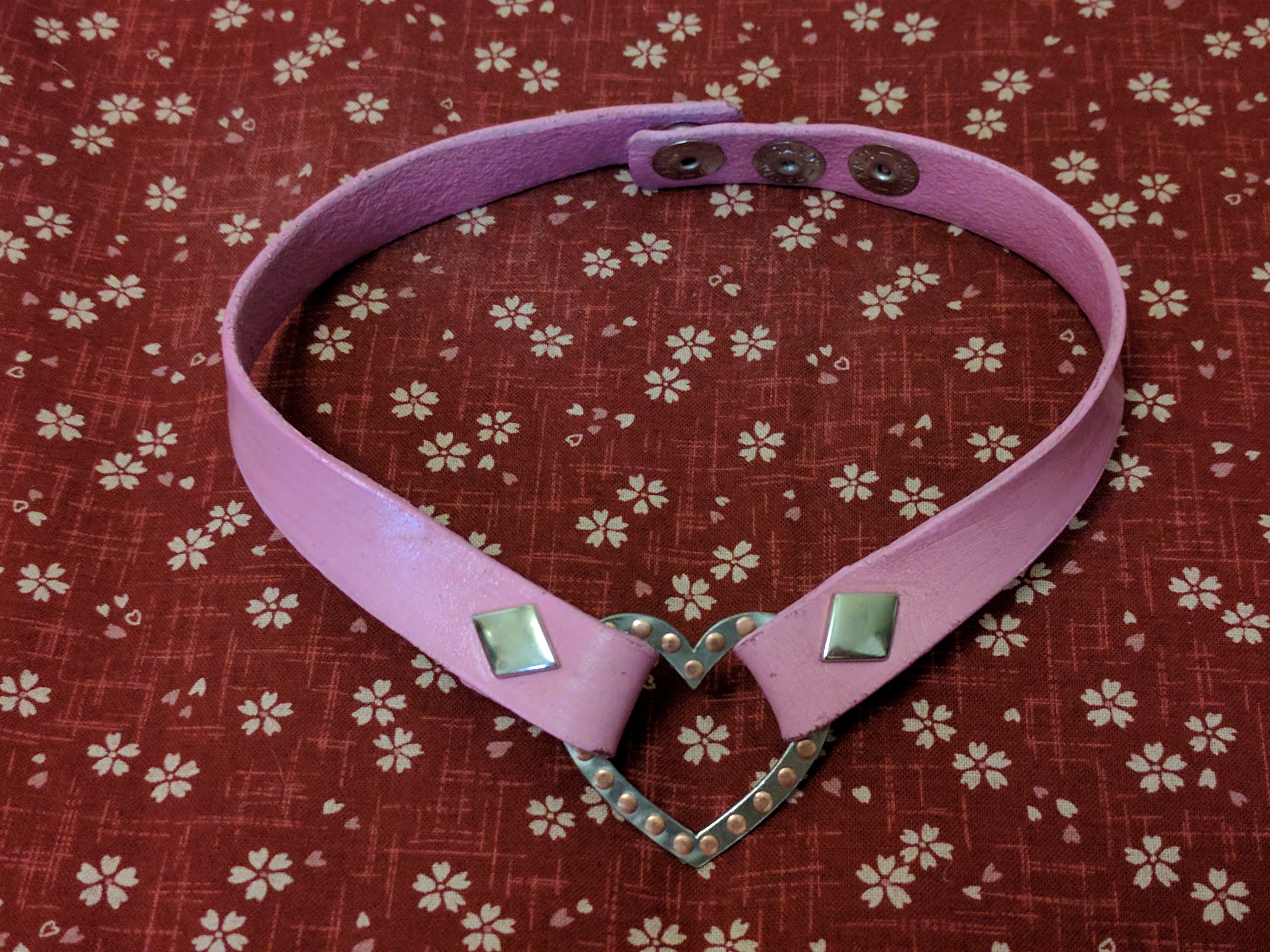 A pink collar with diamond buttons, with a rivetted heart in the middle.
