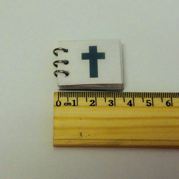 A teensy tiny prayer book sitting on a ruler, three point five centimeters.
