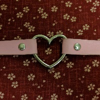 A pink collar with a heart center, laying on a red sakura pattern cloth, little tiny flower pattern.
