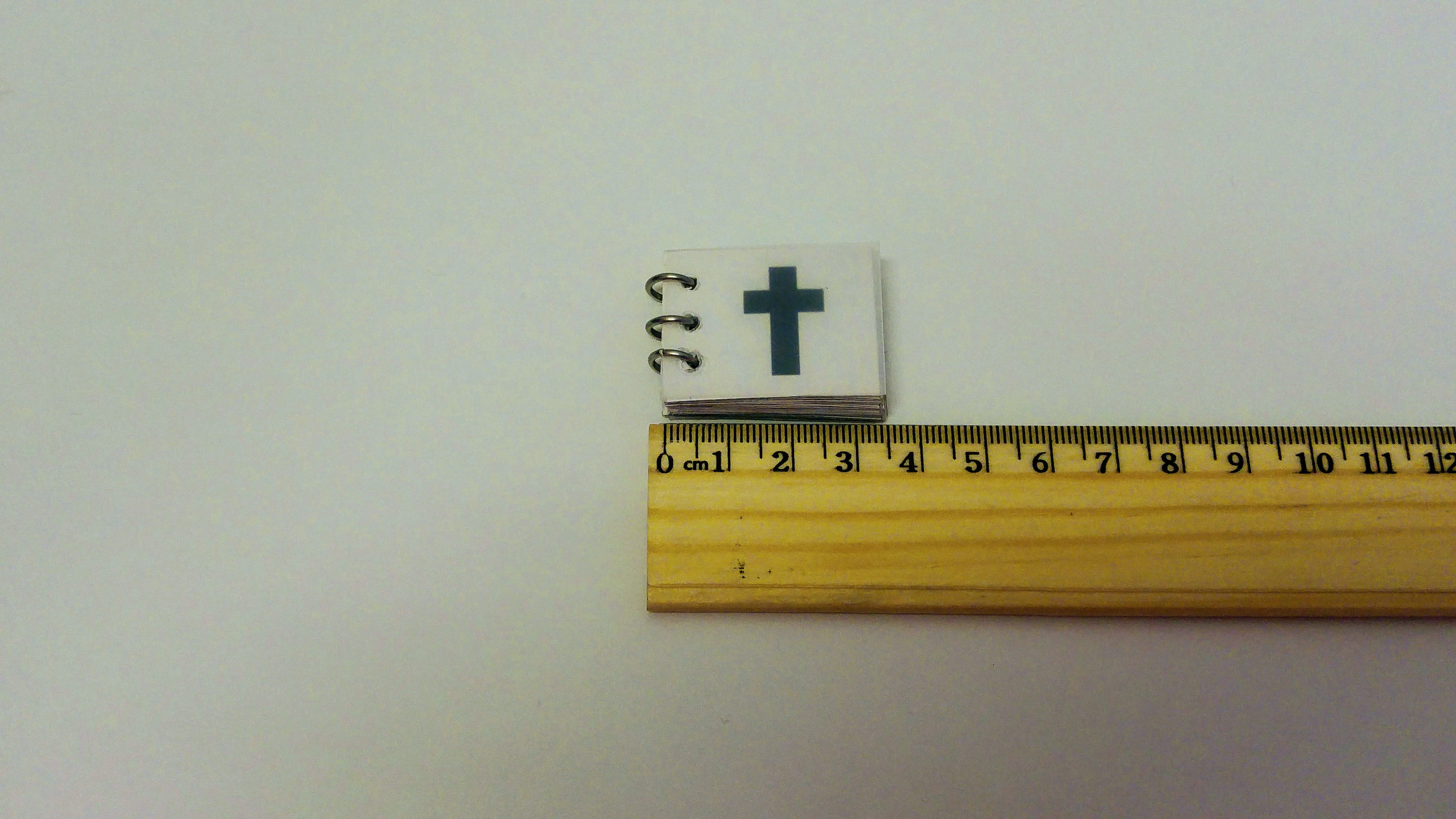 The prayer book on top of a ruler, showing 3.5 centimeters long, so 2.7 by 3.5 centimeters, shown just on a plain table.