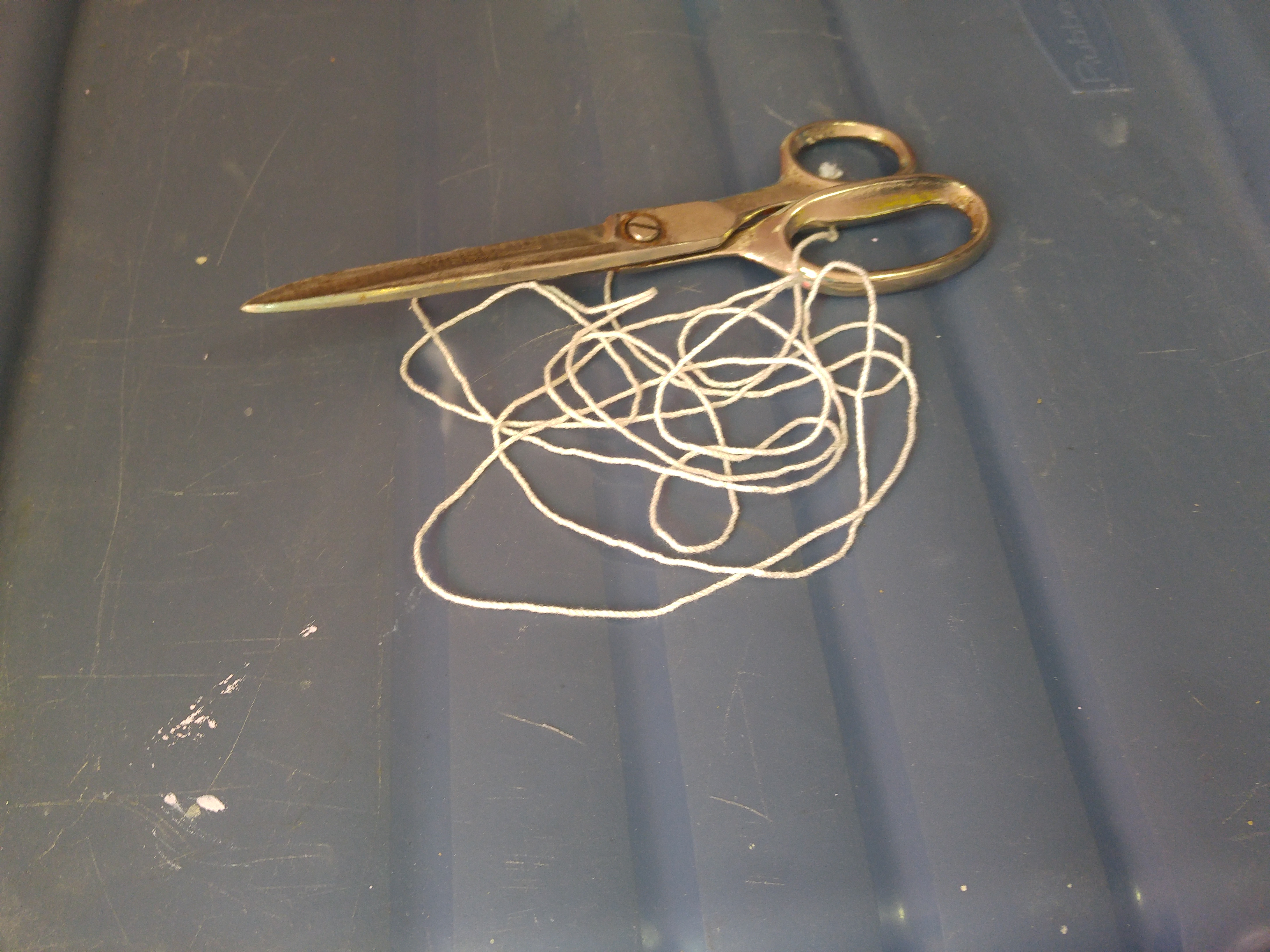 A tangle of string, sitting beside a pair of scissors, just on a plastic bin.
