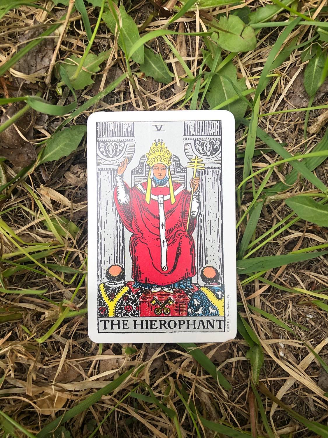 The Heirophant, upright, laying in the grass.