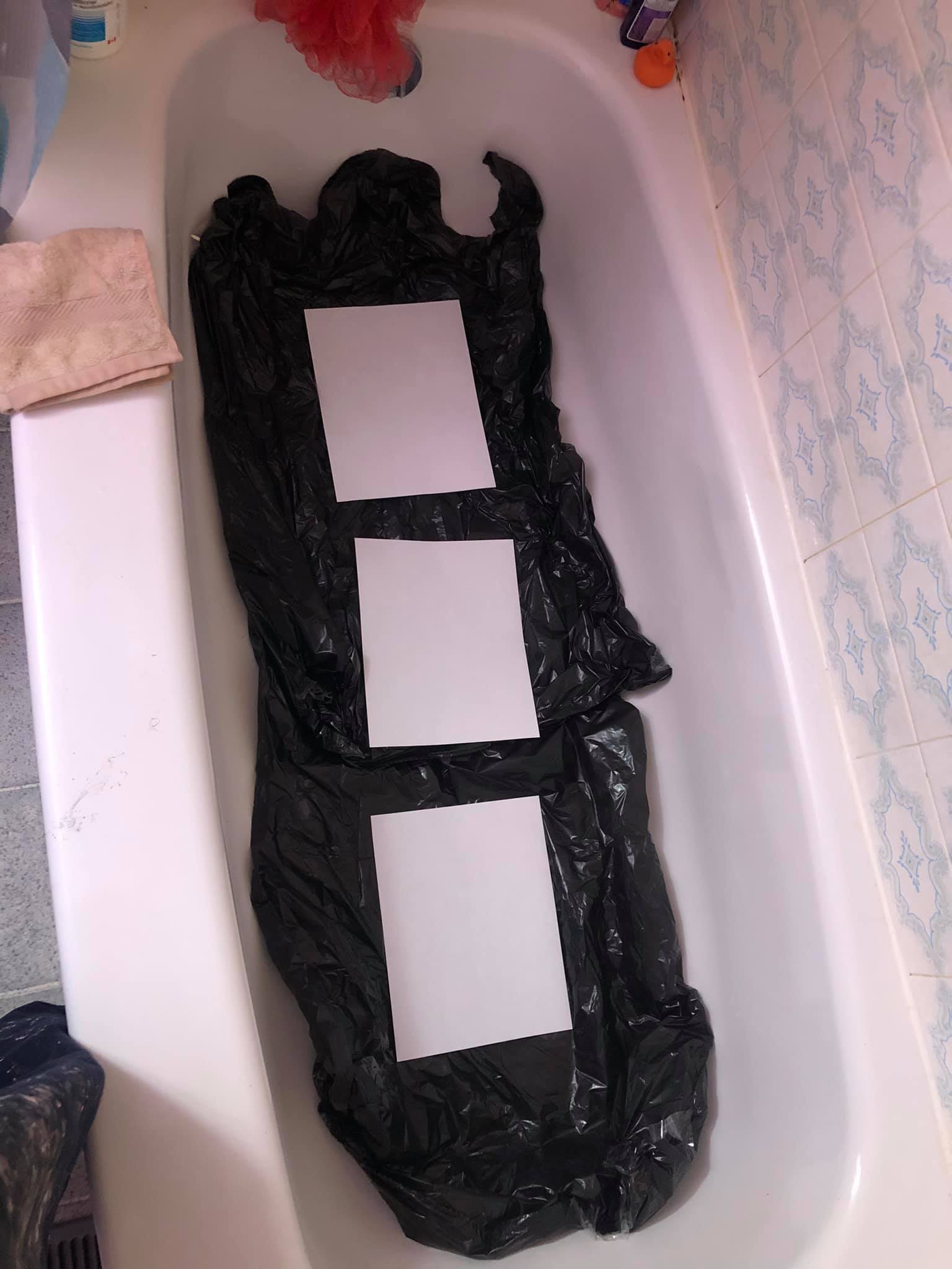 Three canvases lay in a bathtub, with black garbage bags laid out beneath to protect the bottom.