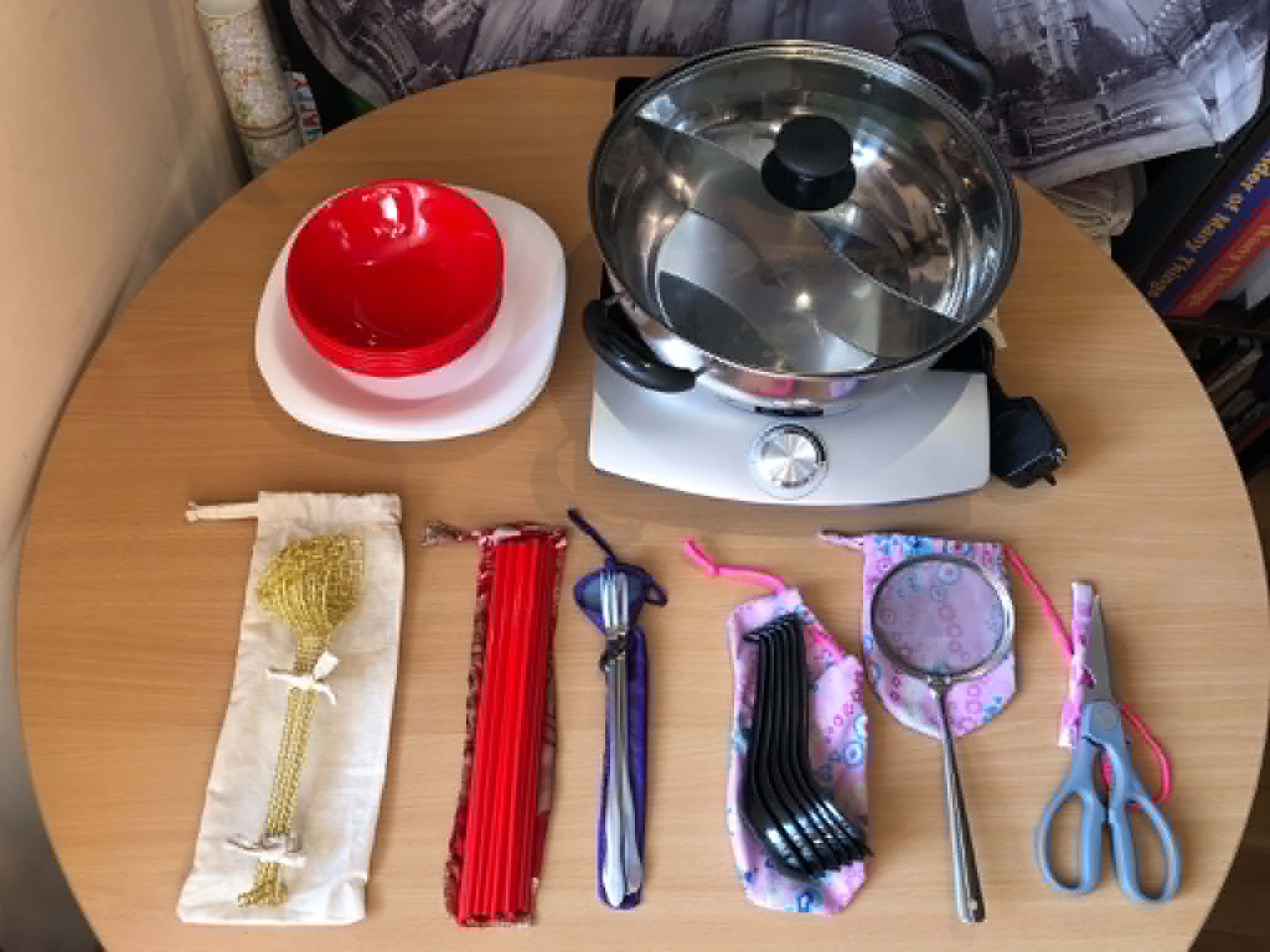 A hotpot setup including ingredient platters, bowls, pot, hob, scoops, chopsticks, spoons, skimmer, scissors and optional forks on top of their respective carry pouches.