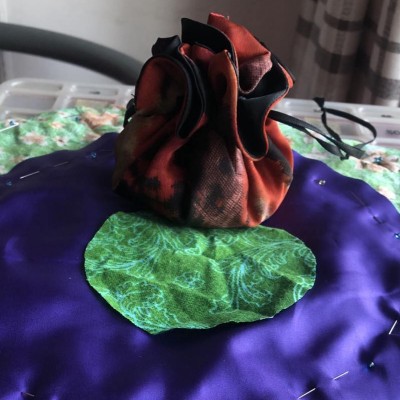 Currently in the initial stages, we have green patterned fabric and shiny purple fabric circles, with the finished earring pouch style bag that we're using as a template above it.