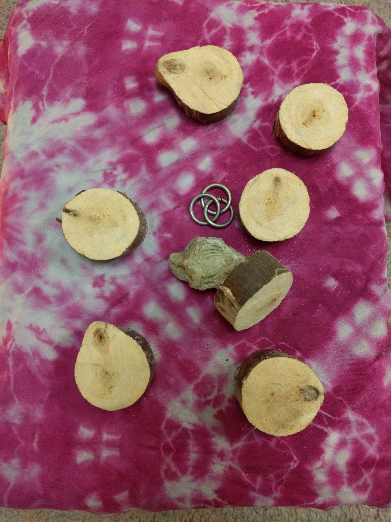 A set of seven wooden disks, a fossilized stone, and three metal rings, on a pink silk pattered cloth.