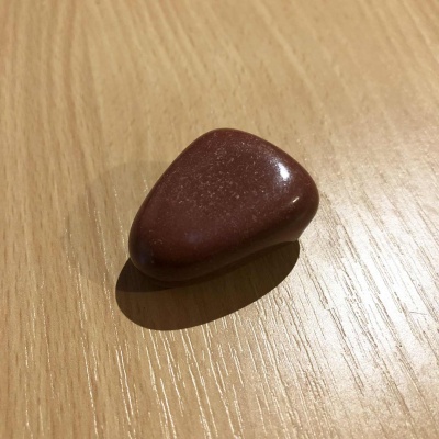 A small reddish brown tumbled stone, sitting on a wooden table.