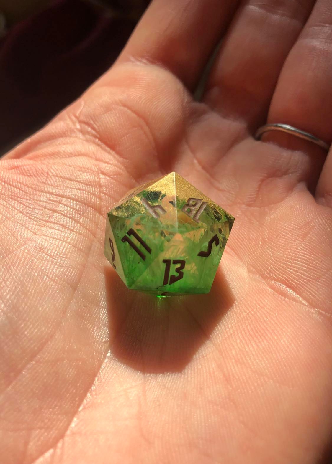 The swampy homemade resin dice with sharp corners, showing the gold on one side, representing the soil, and a murky, swirly green through the middle leading to a more solid green on the other side, representing the swampwater and plantlife inside.