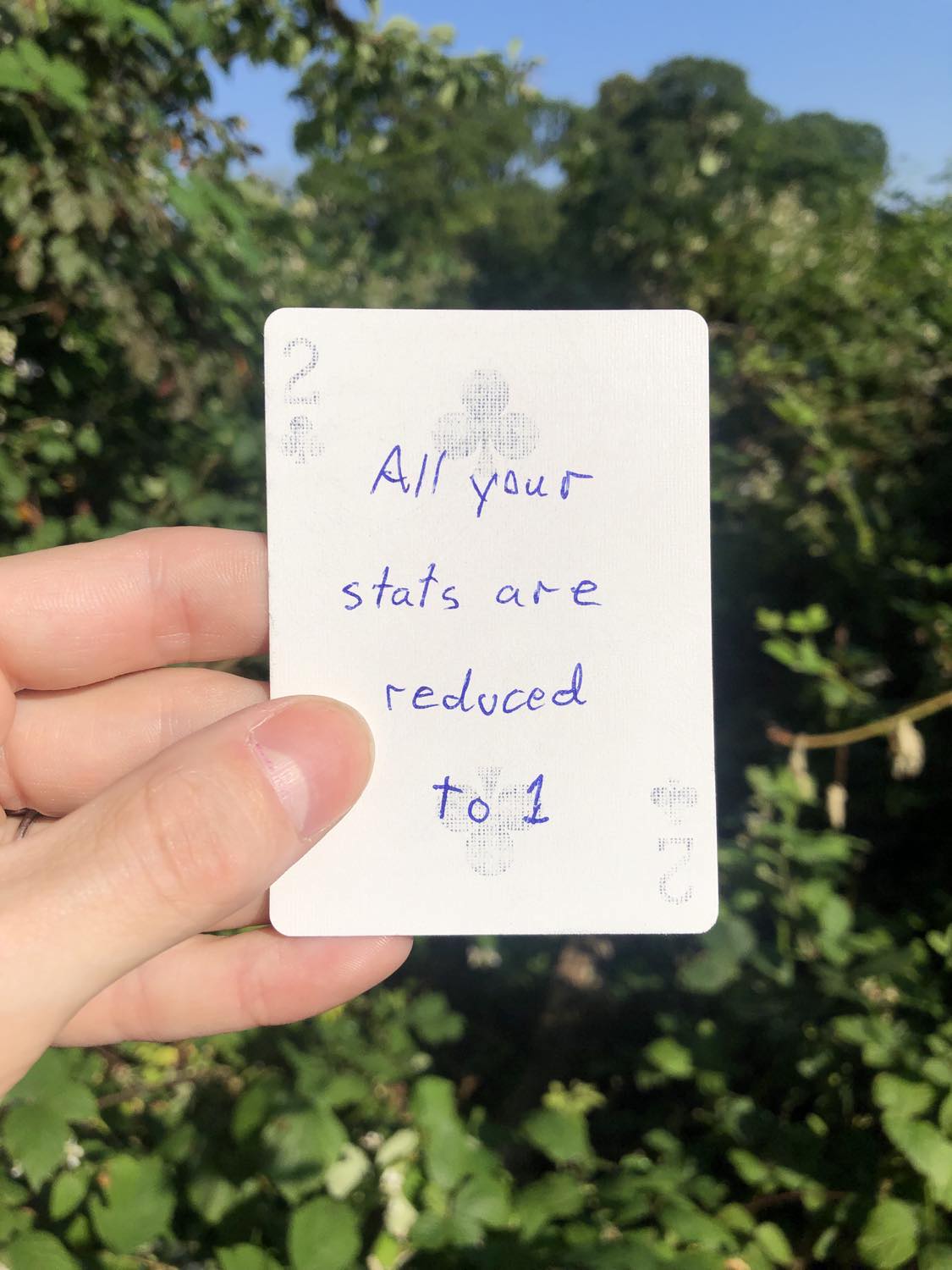The two of clubs, held with the trees and foliage behind. All your stats are reduced to 1.
