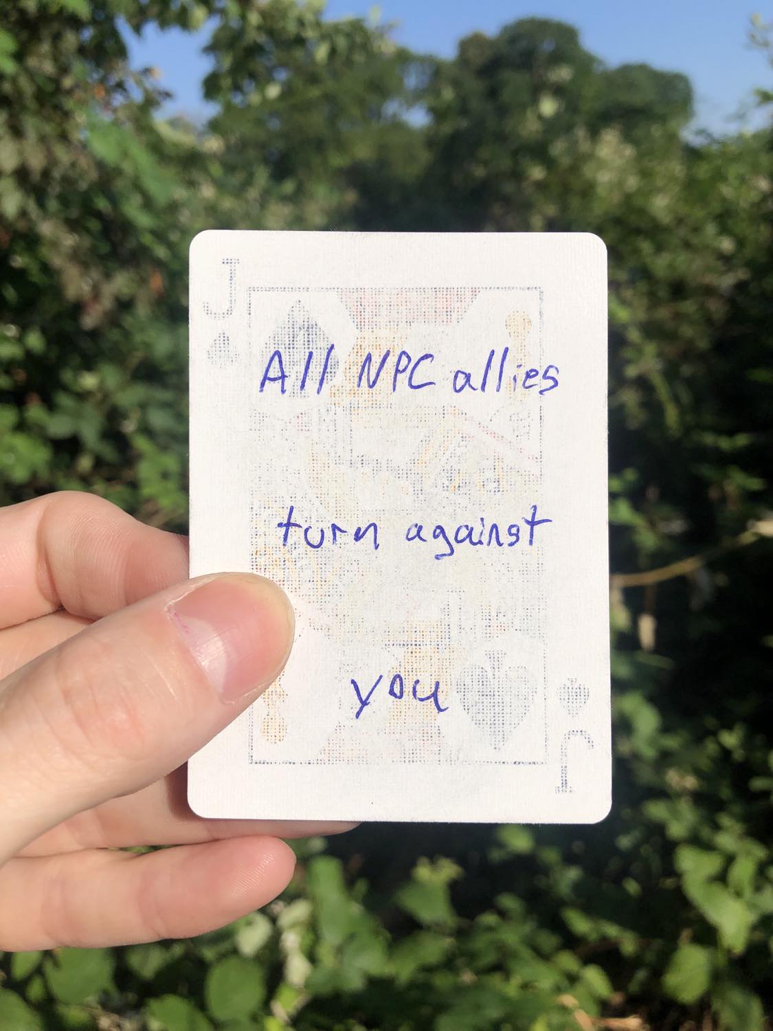 The jack of spades, held with the trees and foliage behind. All NPC allies turn against you.