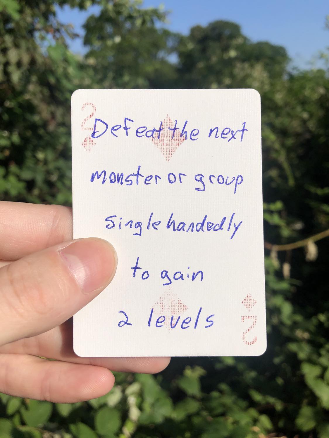 The two of diamonds, held with the trees and foliage behind. Defeat the next monster or group singlehandedly to gain 2 levels.