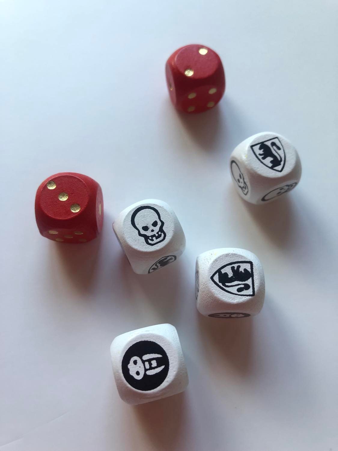 HeroQuest dice, with two red number pip dice (showing a 3 and a 2), and four combat dice, showing a skull, two white shields, and one black shield, sitting on a plain white surface.