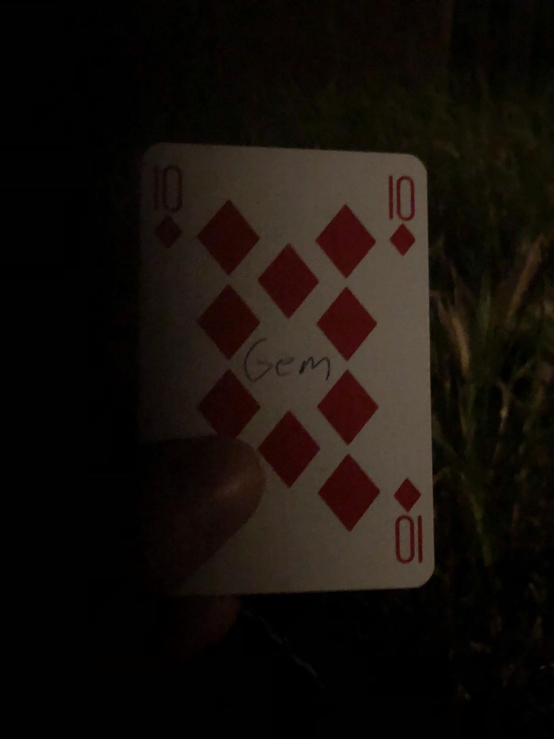 The ten of diamonds with the word Gem written on it, held in the barely lit dark.