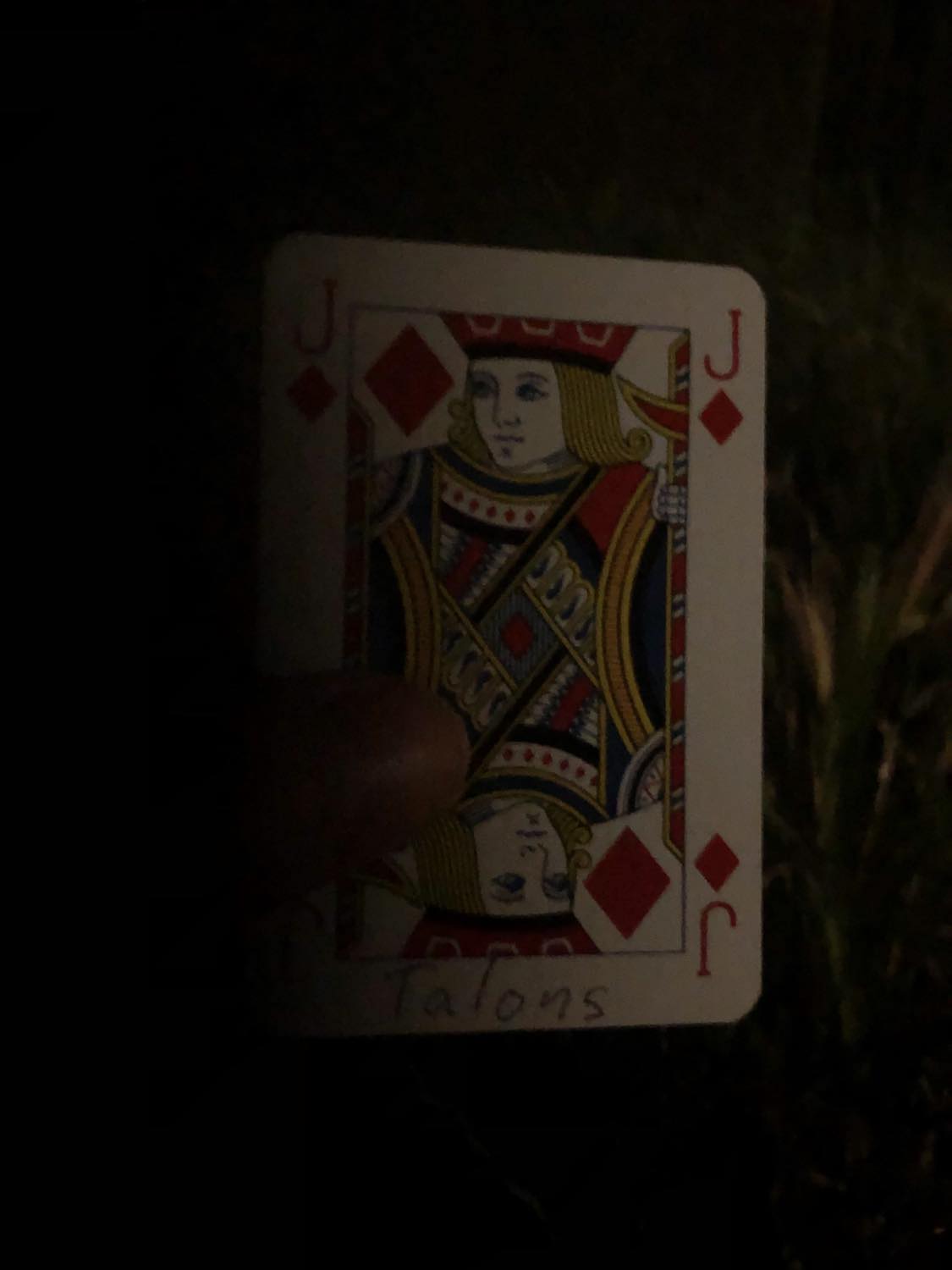 The jack of diamonds with the word Talons written on it, held in the barely lit dark.