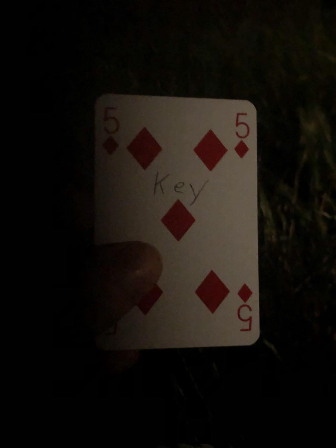 The five of diamonds with the word Key written on it, held in the barely lit dark.