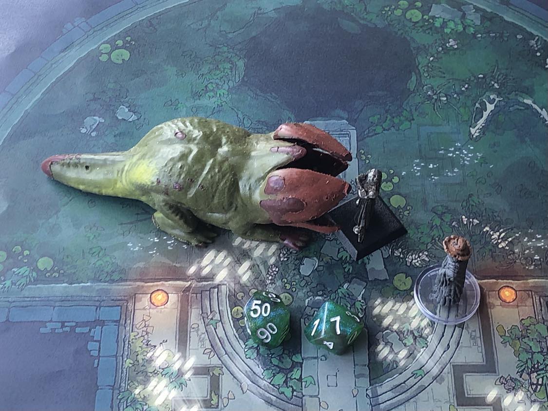 The battle map from above, with the monk fully attacking the creature, and the sorcerer rolling a pair of d10 dice to determine the wild magic surge.