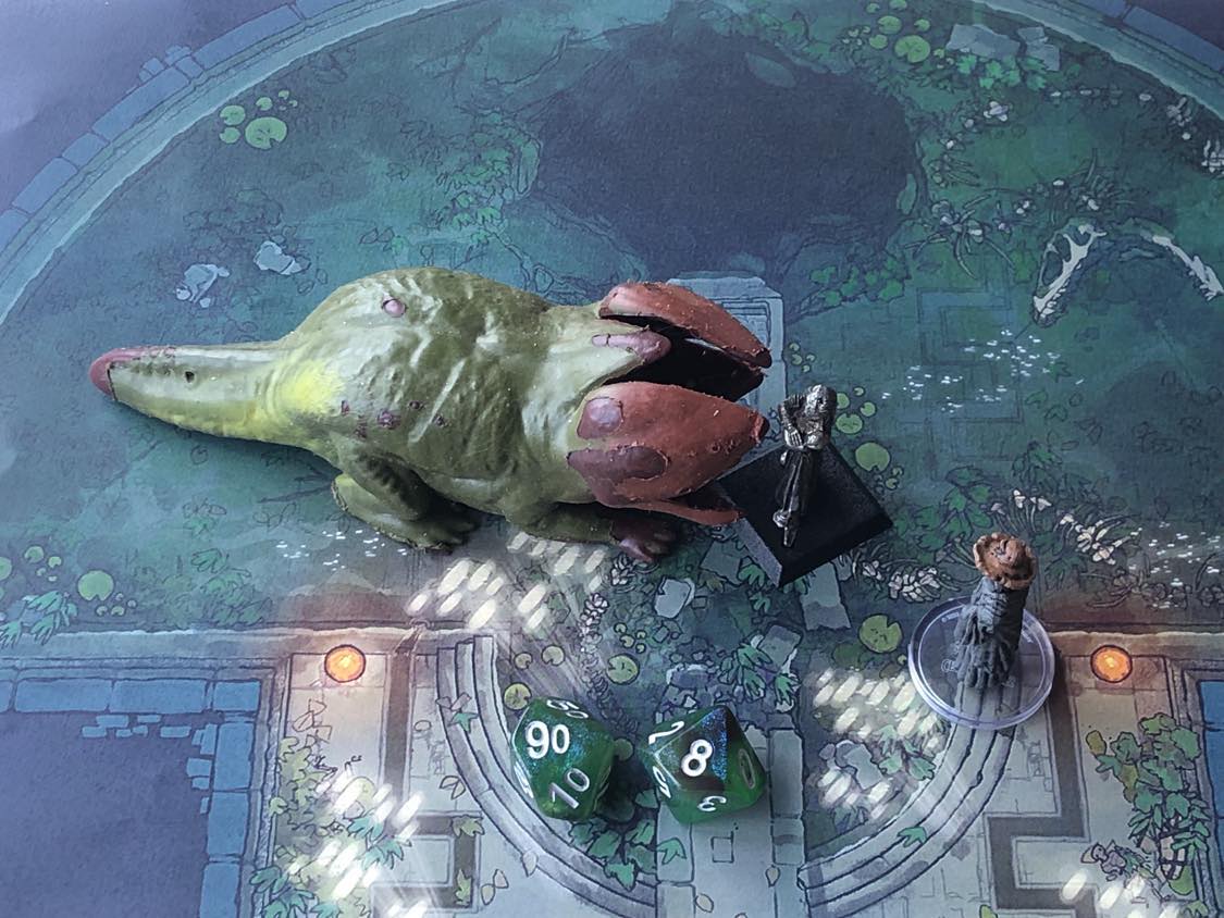 The battle map from above, with the monk fully attacking the creature, and the sorcerer rolling a pair of d10 dice to determine the wild magic surge.